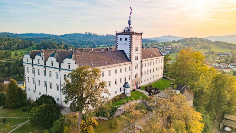 Schloss Weitra, © Benjamin Wald Luftaufnahme von Schloss Weitra in Österreich bei Sonnenuntergang, umgeben von grüner Landschaft und Bäumen.