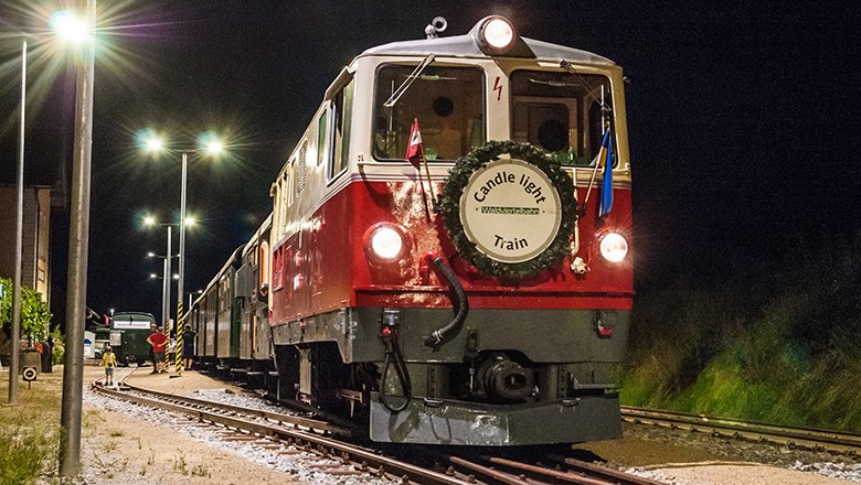 Roter Zug mit wei&szlig;em Frontschild 'Candle light Train' und Krkanz &auml;hrt nachts auf beleuchtetem Gleis