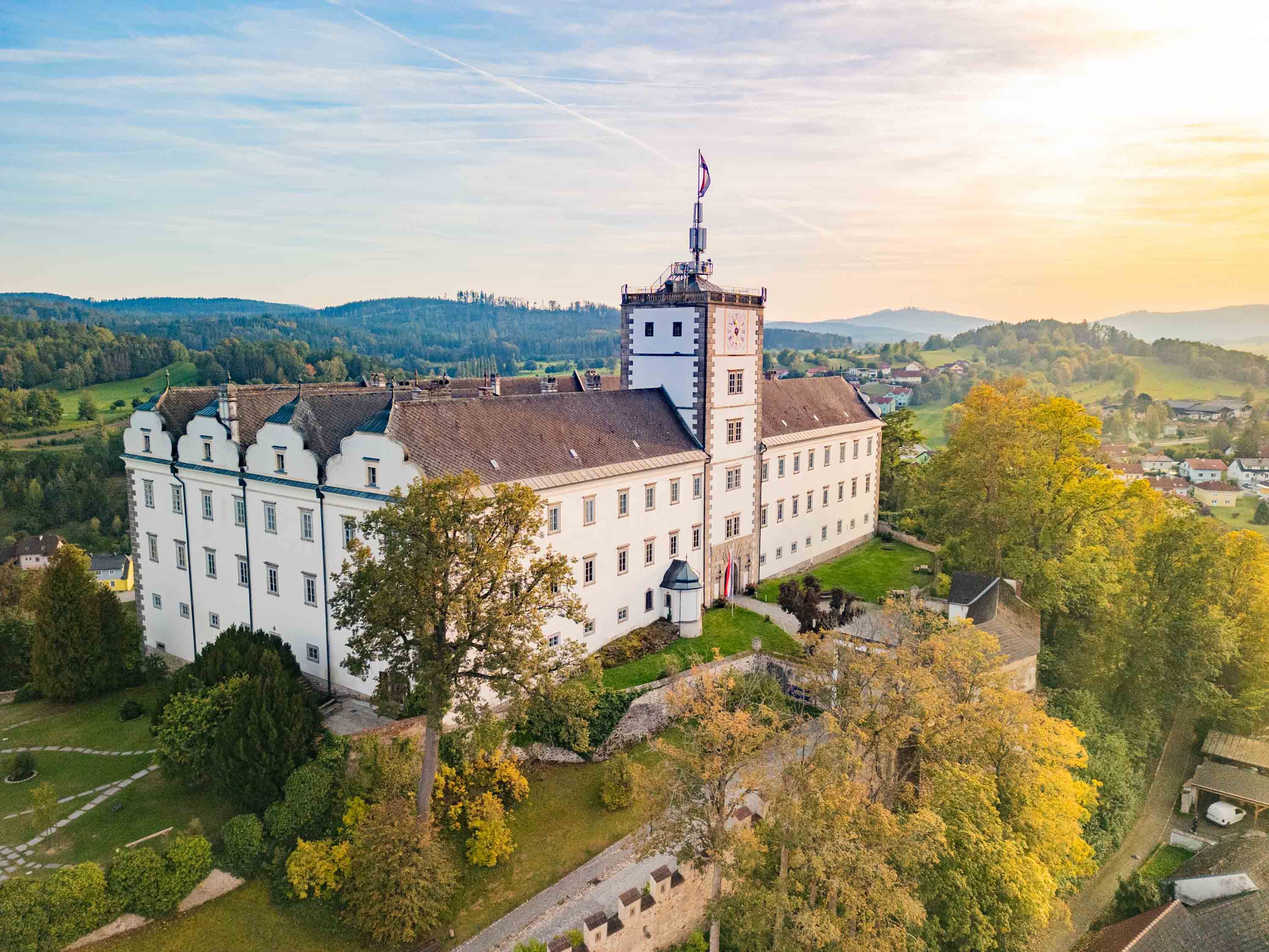Luftaufnahme von Schloss Weitra in Österreich bei Sonnenuntergang, umgeben von grüner Landschaft und Bäumen.