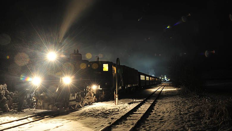 Ein beleuchteter Zug fährt nachts durch eine verschneite Landschaft.