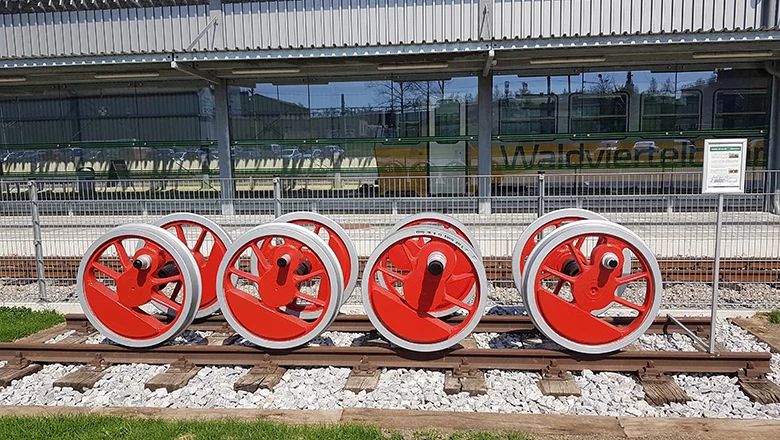 Vier rote Treibräder einer Dampflokomotive als Ausstellungsstück auf einem Gleis vor dem Bahnhof der Waldviertelbahn.