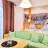Gem&uuml;tliches Doppelzimmer mit zwei Betten, gr&uuml;nem Sofa und gro&szlig;em Wandbild einer Landschaft.