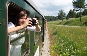 Frau sieht aus dem Waggon der Waldviertelbahn hinaus und fotografiert.