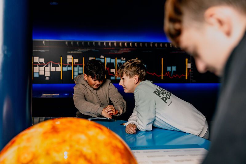 Zwei Jungen interagieren an einem blauen Tisch in einem Wissenschaftszentrum.