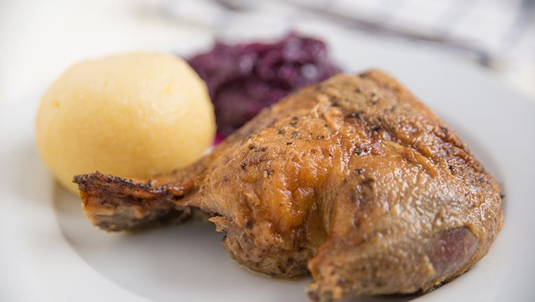Ein Teller mit gebratener Gänsekeule, Kartoffelknödel und Rotkraut.