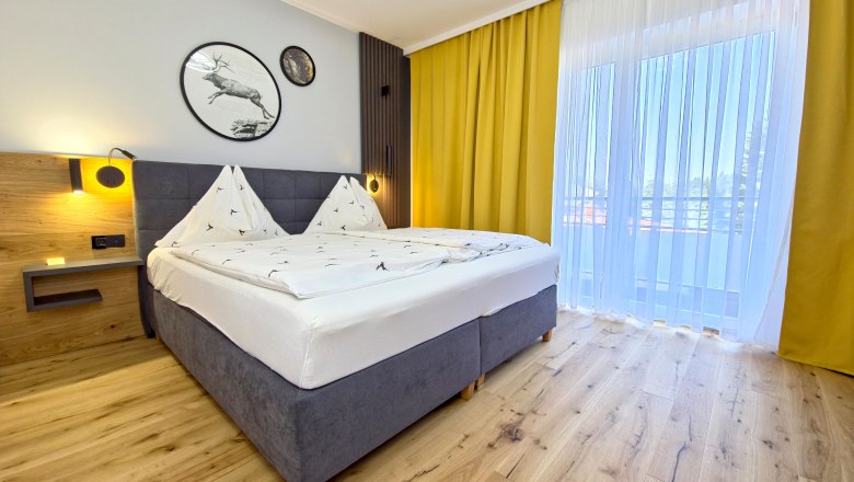 Modern eingerichtetes Schlafzimmer mit Doppelbett, Holzboden und gelben Vorh&auml;ngen.