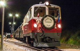 Roter Zug mit wei&szlig;em Frontschild 'Candle light Train' und Krkanz &auml;hrt nachts auf beleuchtetem Gleis