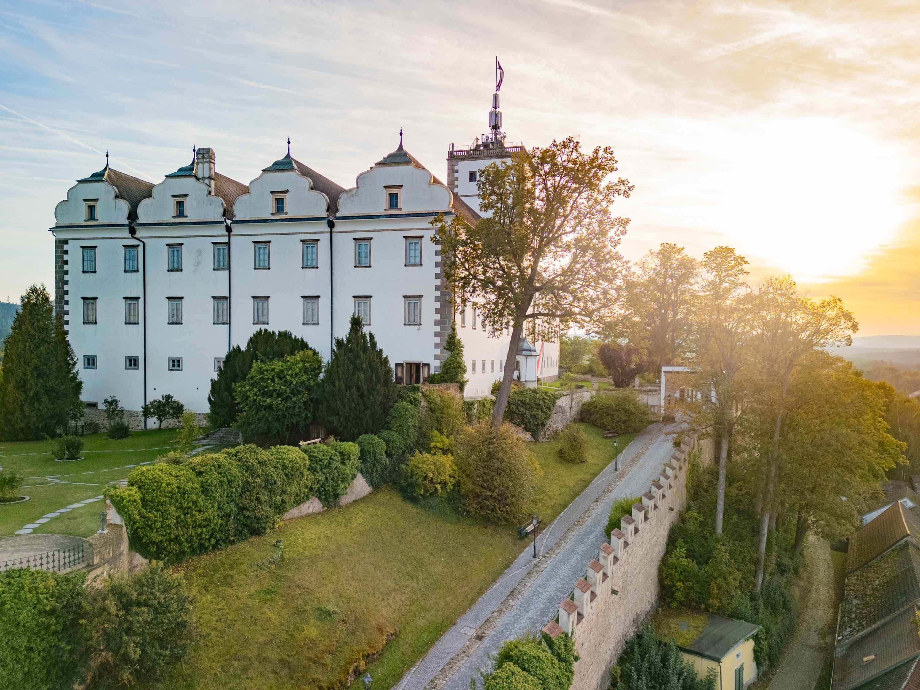 Schloss Weitra bei Sonnenuntergang mit Garten und Bäumen im Vordergrund.
