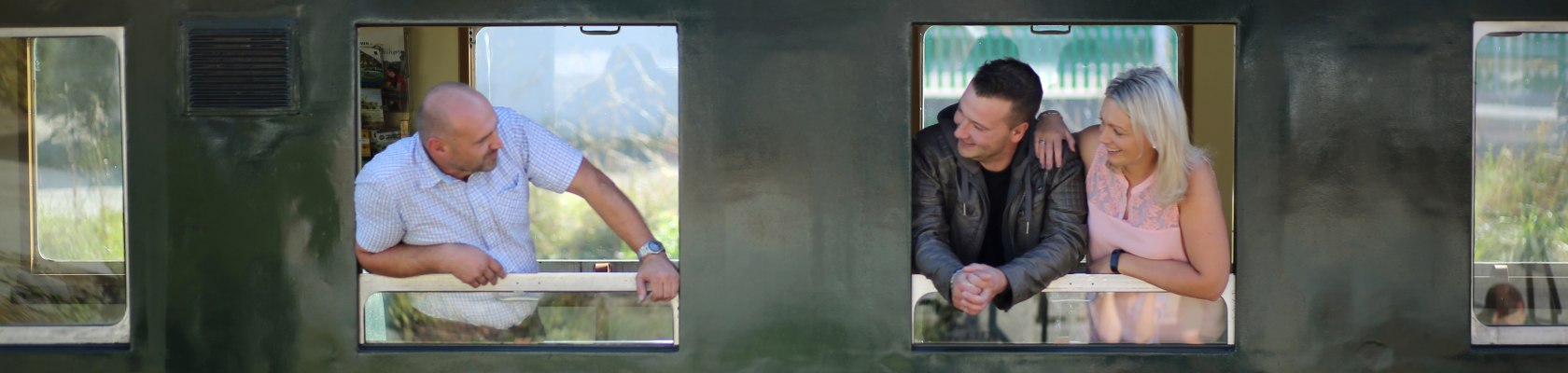 ein Mann lacht zwei weiteren Personen von einem Zugfenster aus zu