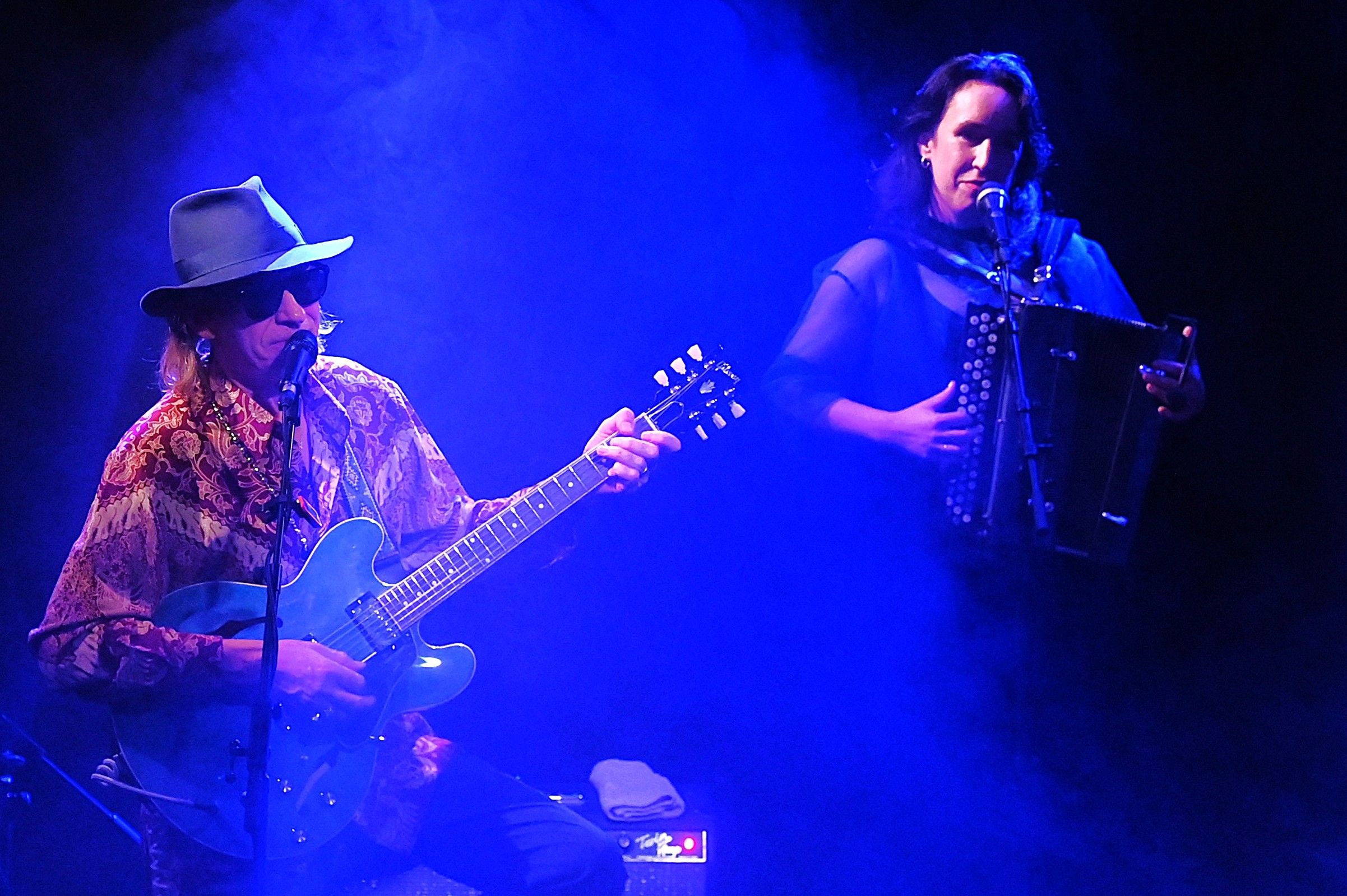 Ernst Molden und Marie-Theres Stickler auf der Bühne: Er spielt Gitarre und singt, sie singt und spielt Akkordeon im blauen Bühnenlicht.