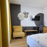 Modern eingerichtetes Zimmer mit gelbem Sessel, Spiegeln an der Wand, einem Fernseher und einem Schreibtisch mit Stuhl.
