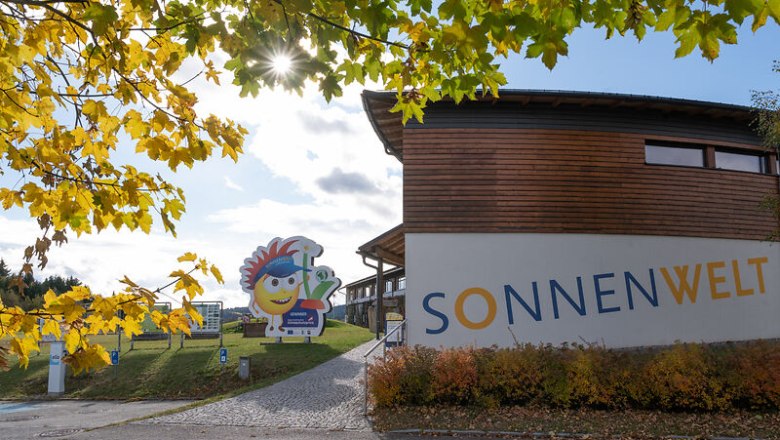 Eingang zur SONNENWELT Gro&szlig;sch&ouml;nau mit herbstlichen B&auml;umen und Sonnenschein.