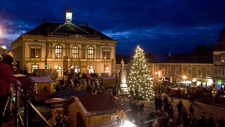 Weihnachtsmarkt bei Nacht mit beleuchtetem Weihnachtsbaum und historischem Rathausgebäude im Hintergrund