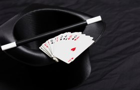 Ein schwarzer Zylinderhut mit einem Zauberstab und einem F&auml;cher aus Spielkarten darauf.