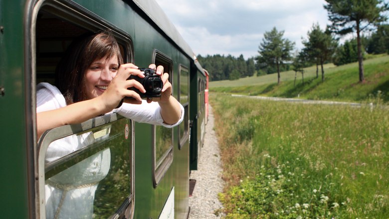 Frau sieht aus dem Waggon der Waldviertelbahn hinaus und fotografiert.