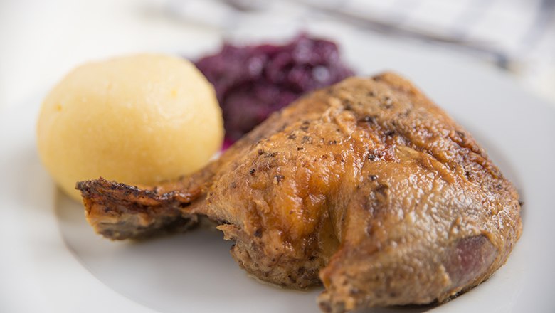 Ein Teller mit gebratener G&auml;nsekeule, Kartoffelkn&ouml;del und Rotkraut.